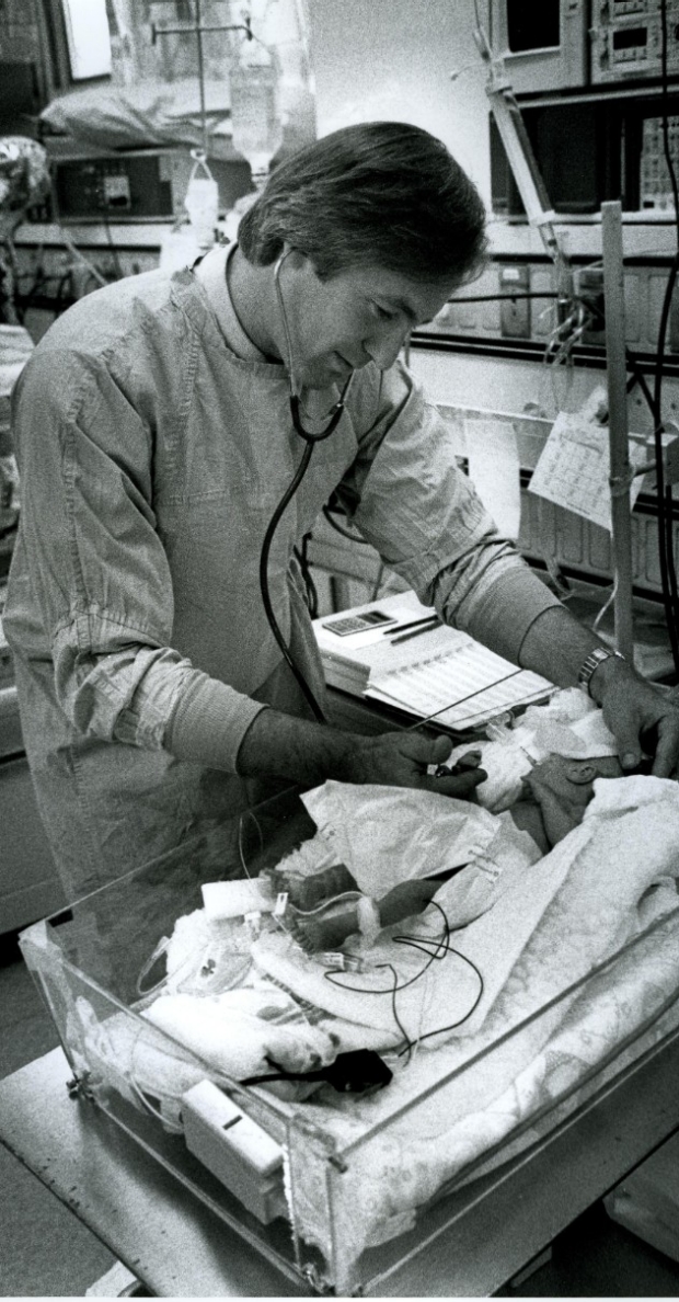 A black and white photo of Dr. David Stevenson caring for infant in the NICU in the 1980s